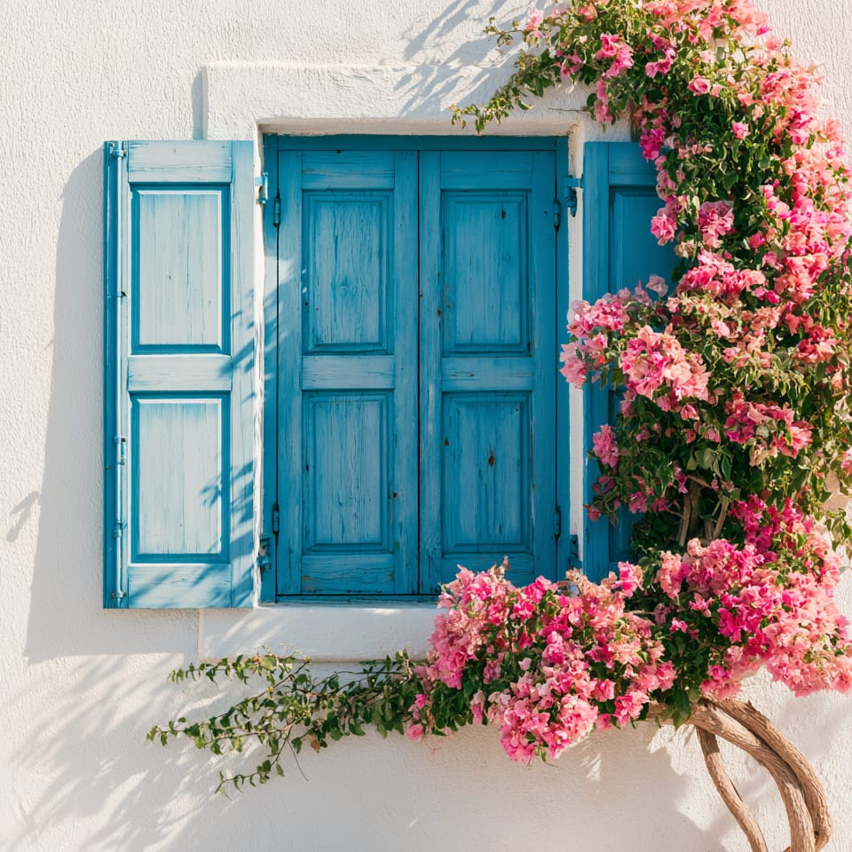 White stucco wall with blue shutters and vibrant pink bougainvillea climbing around a window.