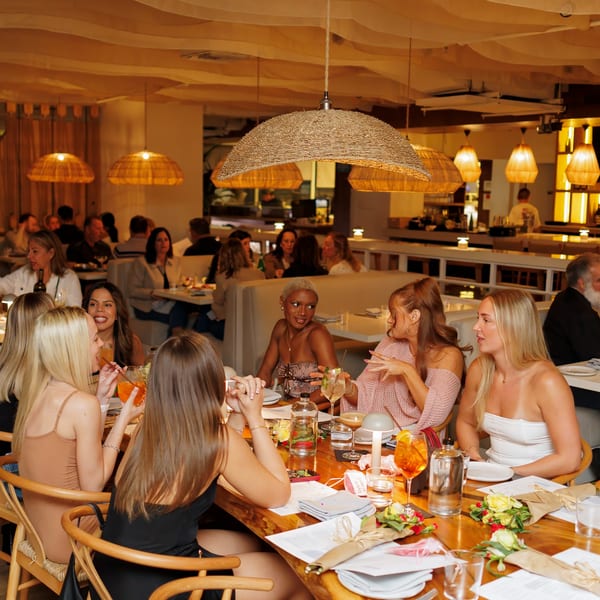 Diners enjoying a meal in a warmly lit restaurant with woven pendant lights and a bar.